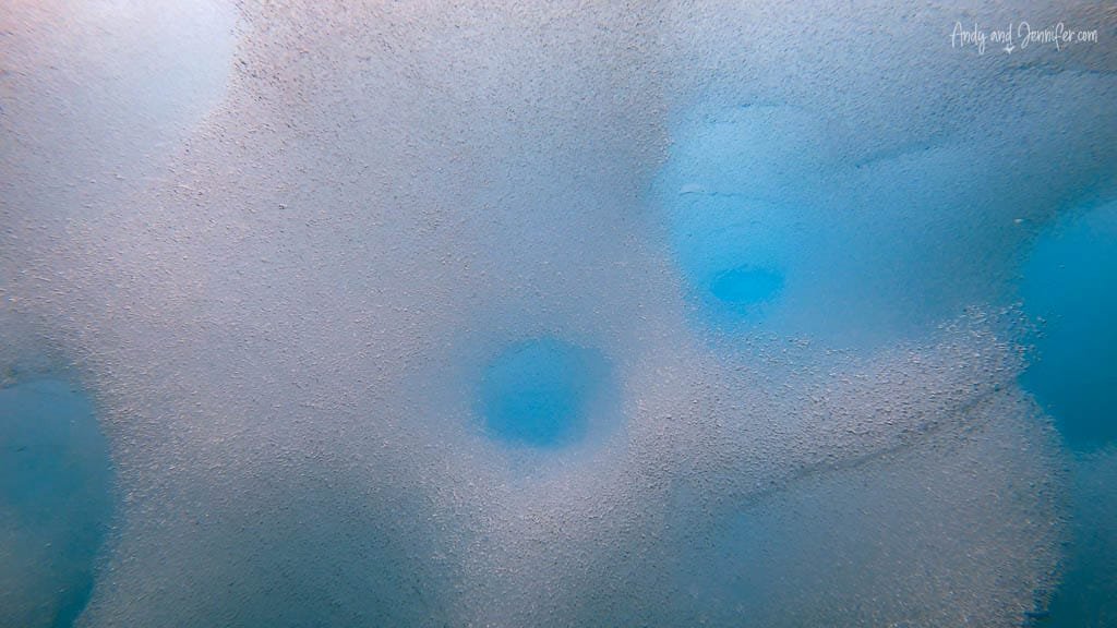 Close-up underwater view of submerged iceberg with textured surface, surrounded by deep blue water.
