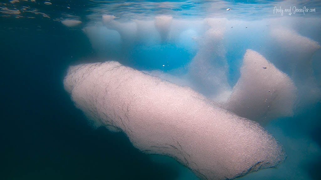 Underwater view of submerged iceberg with textured surface, surrounded by deep blue water.
