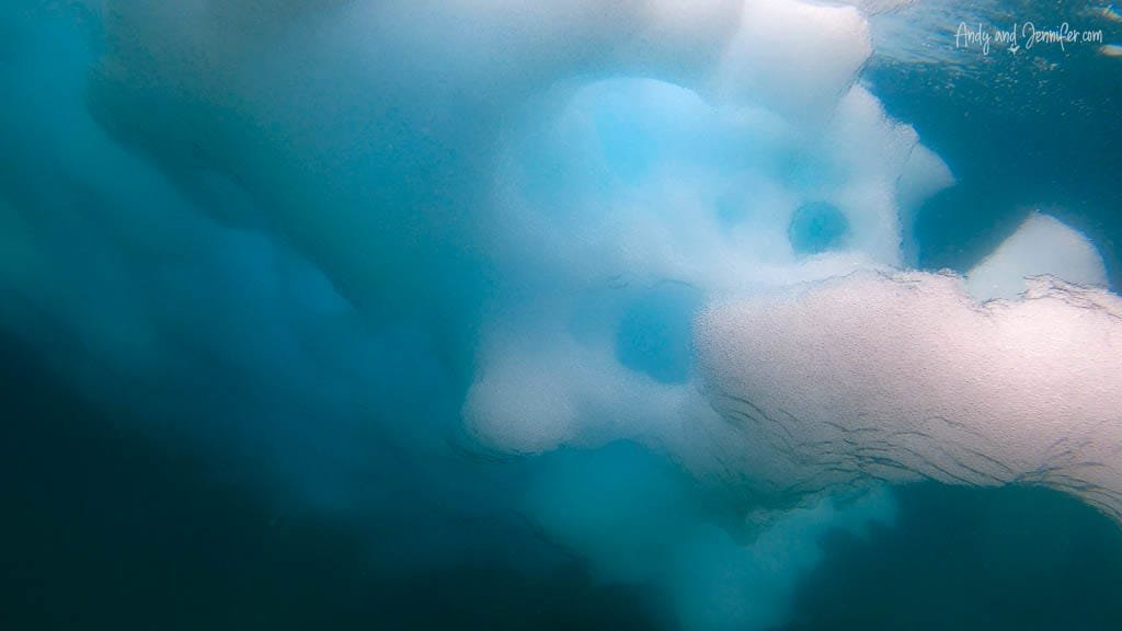 Underwater view of submerged iceberg with textured surface, surrounded by deep blue water.