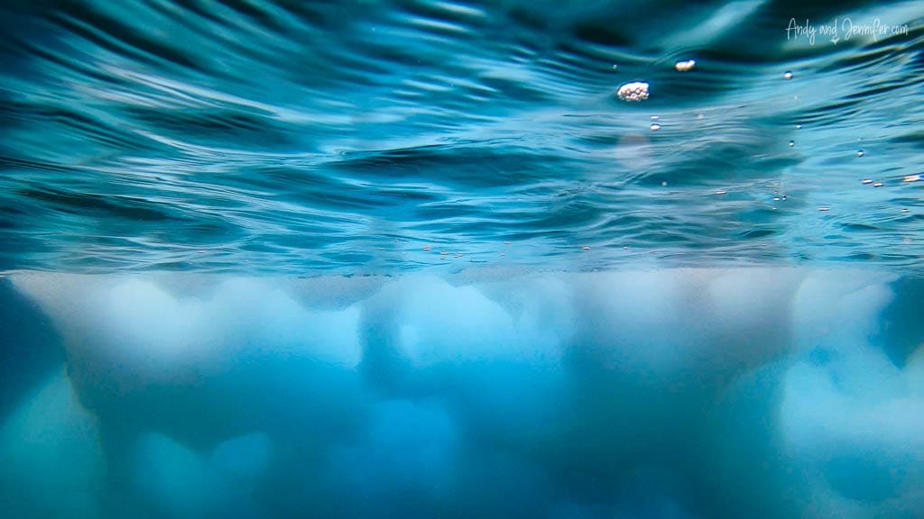 Underwater view of submerged iceberg with textured surface, surrounded by deep blue water.
