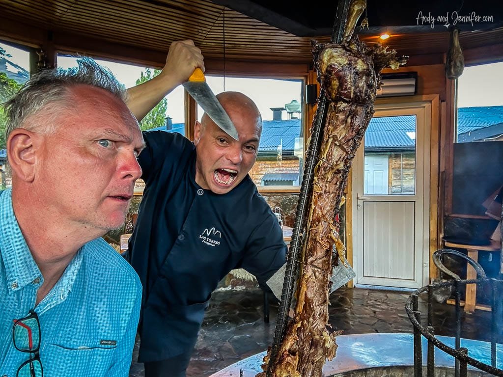 Chef playfully brandishing knife near roasted meat with amused guest