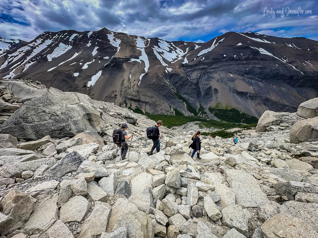 Hikers navigating rocky terrain with snow-capped mountains in the background