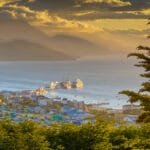Golden hour over Ushuaia with docked ships, colorful rooftops, and distant mountains.