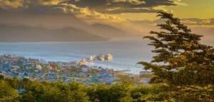Golden hour over Ushuaia with docked ships, colorful rooftops, and distant mountains.