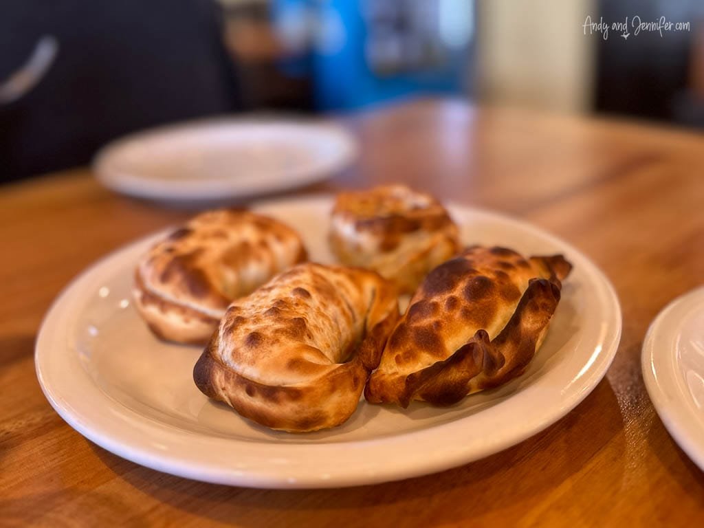 Plate of golden-brown baked empanadas on a wooden table. 