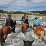 Horseback riders crossing a shallow river in the mountains