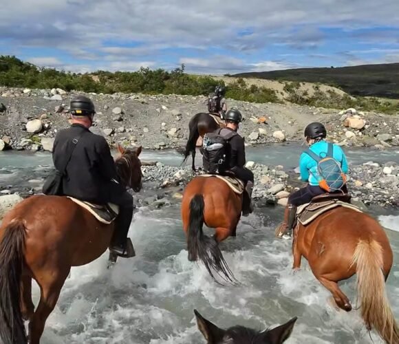 Horseback riders crossing a shallow river in the mountains