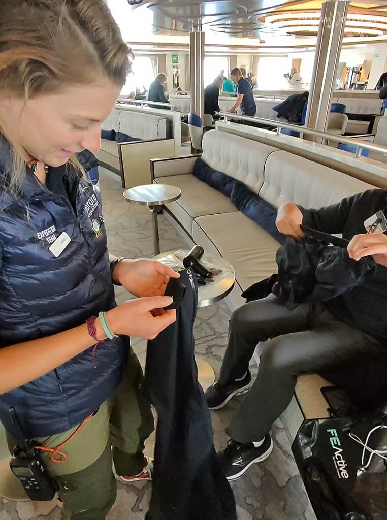  Expedition team member cleaning cold-weather gear to passengers inside a cruise ship lounge, preparing them for an Antarctic adventure.