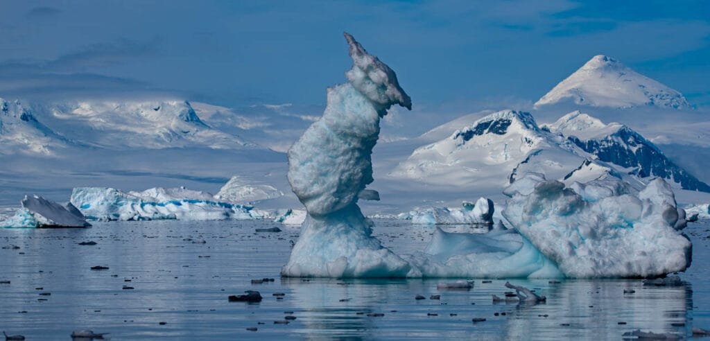 Icebergs floating in Antarctic waters with towering snow-covered mountains in the background.