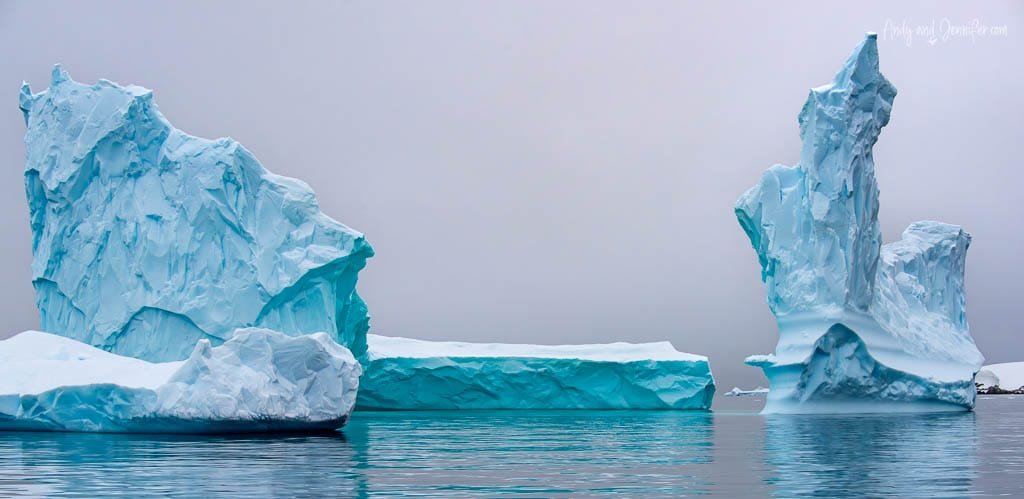 Massive blue icebergs floating in calm Antarctic waters against a foggy sky.