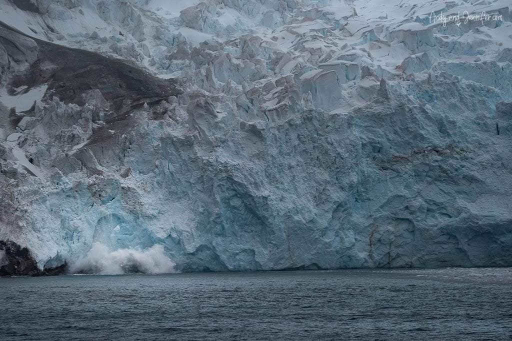 Close-up of a massive glacier meeting the ocean, with chunks of ice breaking off into the water.