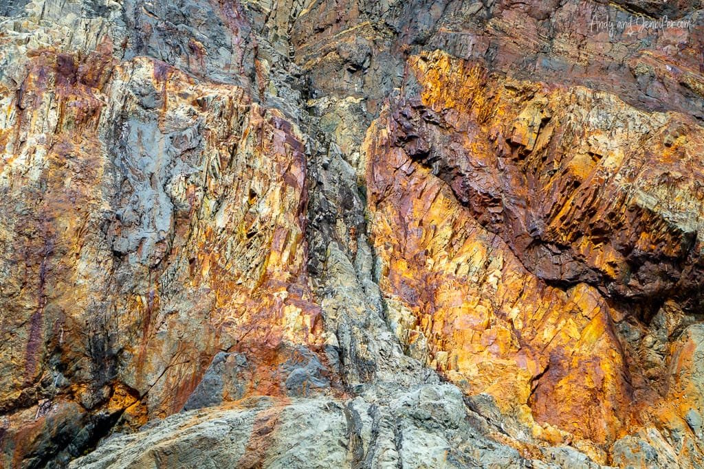 Close-up of a weathered rock formation with striking hues of orange, yellow, red, and gray. 