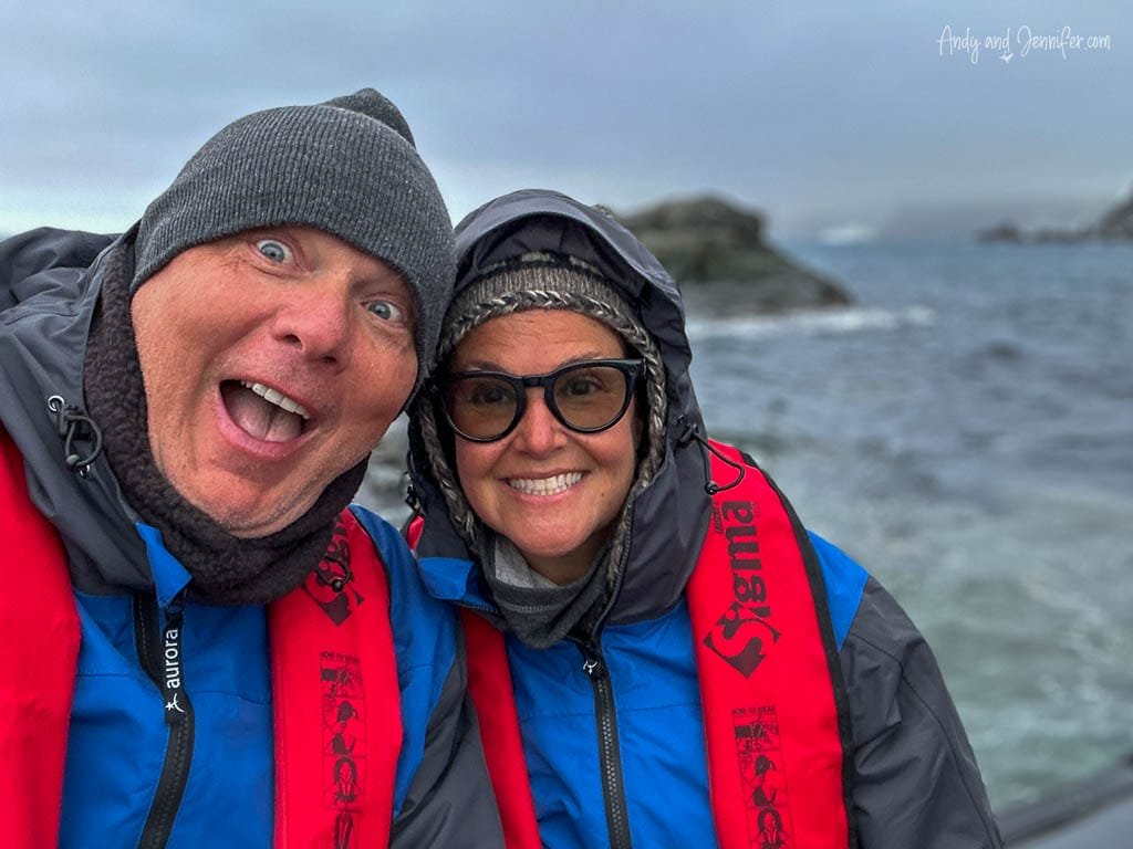  Two smiling people in winter jackets and life vests taking a selfie near the ocean on a foggy day
