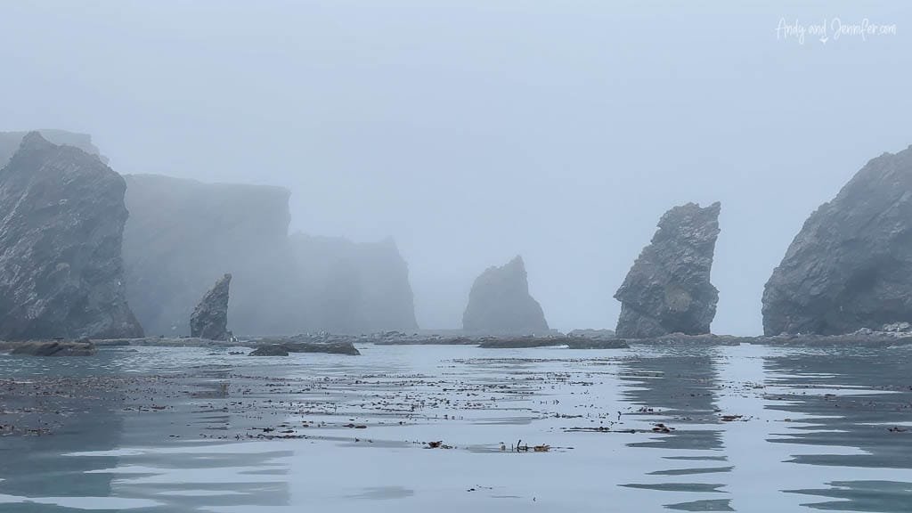 Misty seascape with large jagged rock formations rising from the calm water.