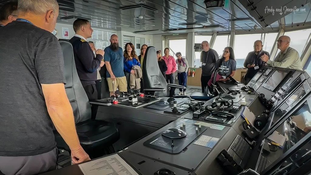  Tour group inside a ship's control room, listening to a uniformed officer explain the navigation equipment.
