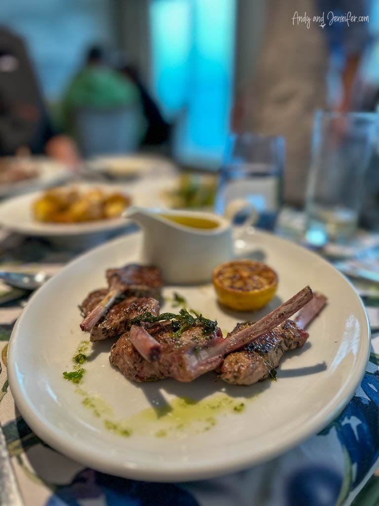 Grilled lamb chops garnished with herbs, served with a roasted lemon and sauce on a white plate.
