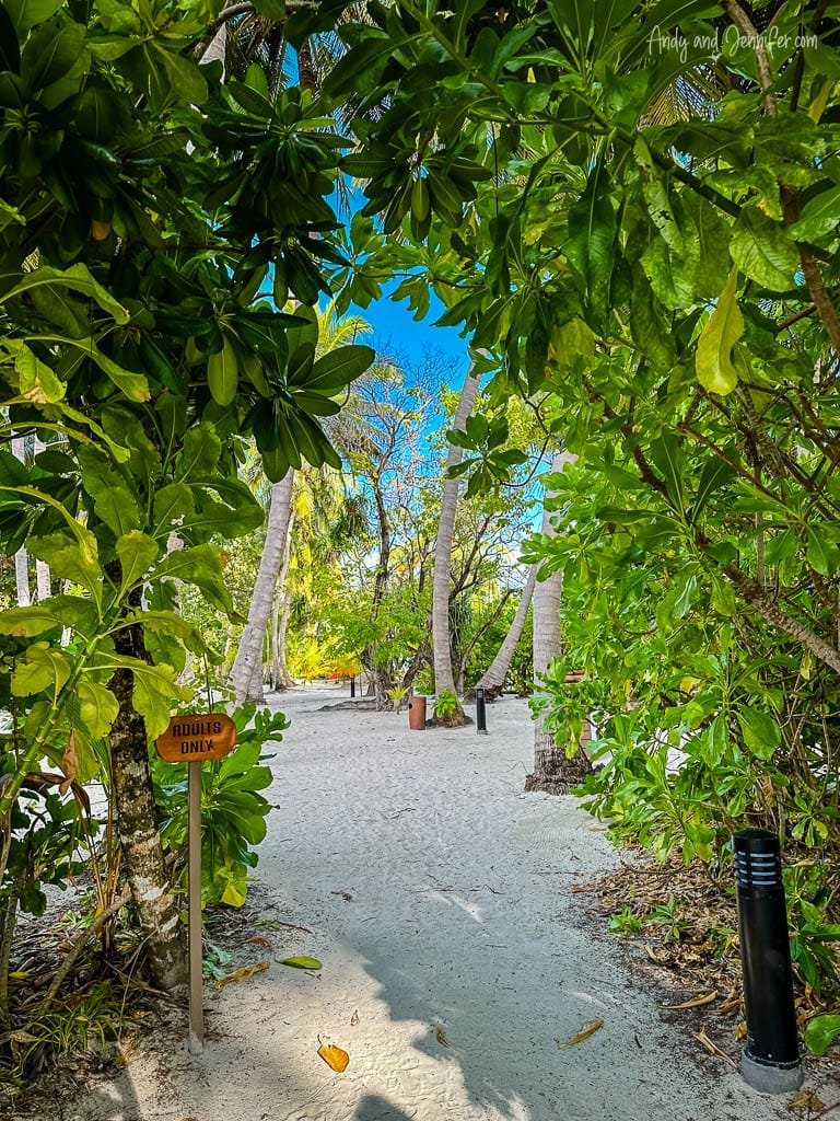 Sandy path through lush tropical greenery with "Adults Only" sign.