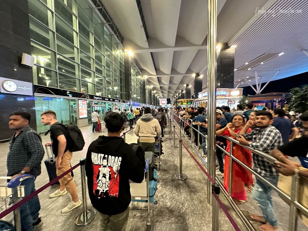Busy airport terminal in Bangalore, India with travelers in long queues at departures.