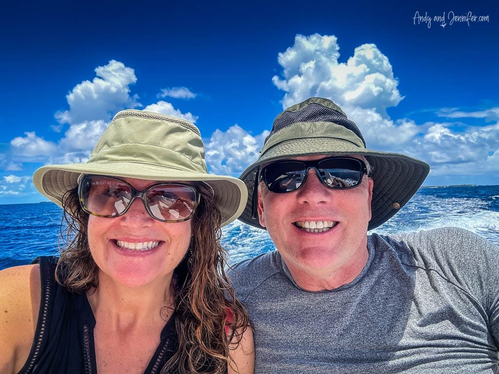 Couple in hats smiling on a boat ride under a bright blue sky.