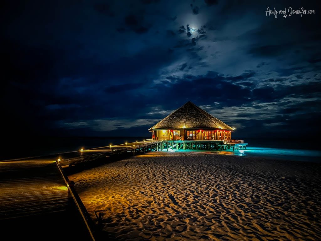 Overwater restaurant lit up at night under a cloudy sky.