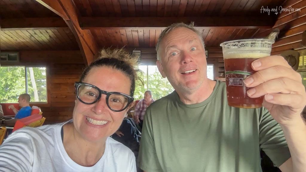 Smiling couple indoors, one holding up a glass of beer in a wooden cabin