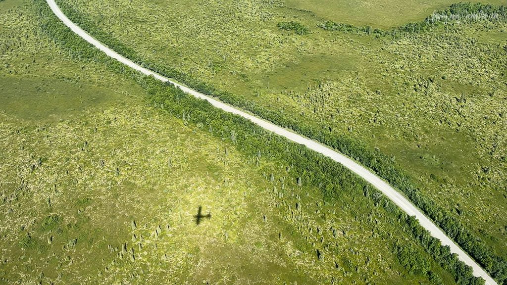 Plane shadow cast over a winding road through green fields