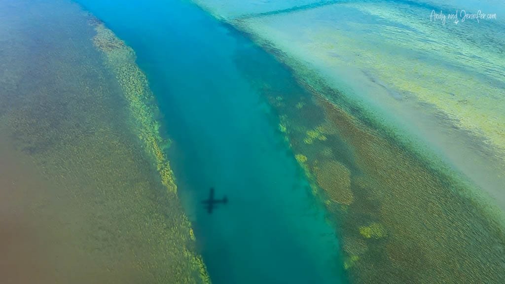 Plane shadow visible over clear turquoise water.