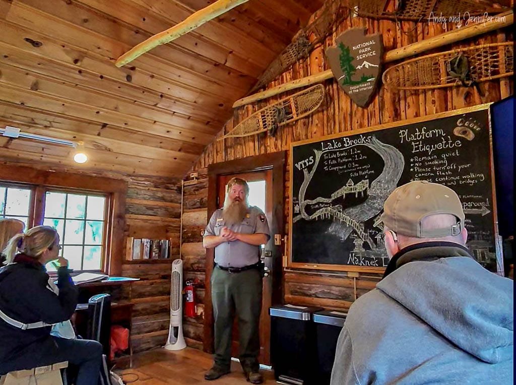 Park ranger giving a talk inside a log cabin with a chalkboard map