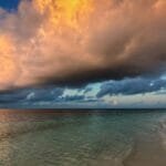 Beach at Vilemendhoo in the Maldives at sunset with dramatic orange and gray clouds over calm ocean.
