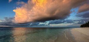 Beach at Vilemendhoo in the Maldives at sunset with dramatic orange and gray clouds over calm ocean.