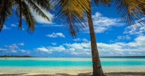 A palm tree framing the crystal-clear turquoise waters of Aitutaki’s lagoon under a bright blue sky.