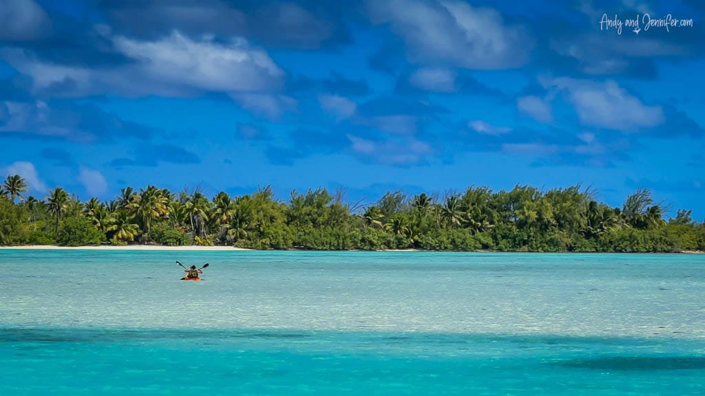 Kayaking across Aitutaki's shallow turquoise lagoon with lush greenery in the background.