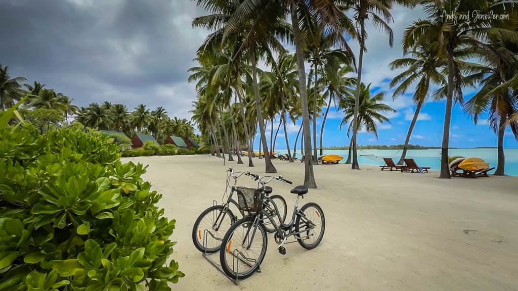 Bicycles resting on the white sandy beach of Aitutaki, surrounded by swaying palm trees and turquoise lagoon views.