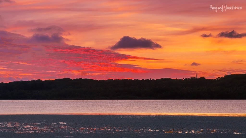 A fiery sunset over the serene waters of Rarotonga, painting the sky in vivid hues of red and orange