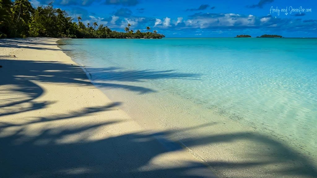 Shadows of palm trees cast over a pristine white sand beach and turquoise lagoon in Aitutaki.