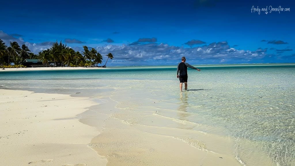 Walking along the shallow, crystal-clear waters of Aitutaki's lagoon with palm trees in the distance.