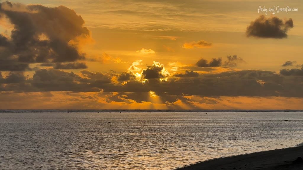 Golden sunset over calm ocean with sunbeams through clouds.