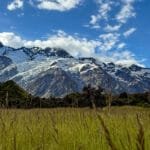 Snowy mountain peaks rising above green valley and grassy field