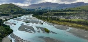 Winding river with sandbanks, green hills, and distant mountains under a cloudy sky.