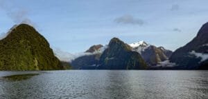Serene fjord with forested cliffs, snow-capped peaks, and low-lying clouds