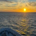 Ship's bow facing an open sea at sunset with orange skies