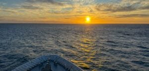 Ship's bow facing an open sea at sunset with orange skies