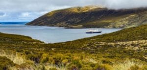 Cruise ship anchored in a calm bay surrounded by green hills