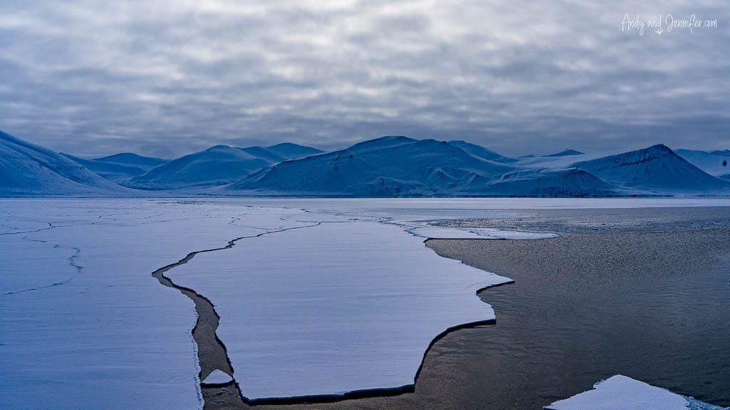 Cracked sea ice in Arctic fjord under cloudy sky