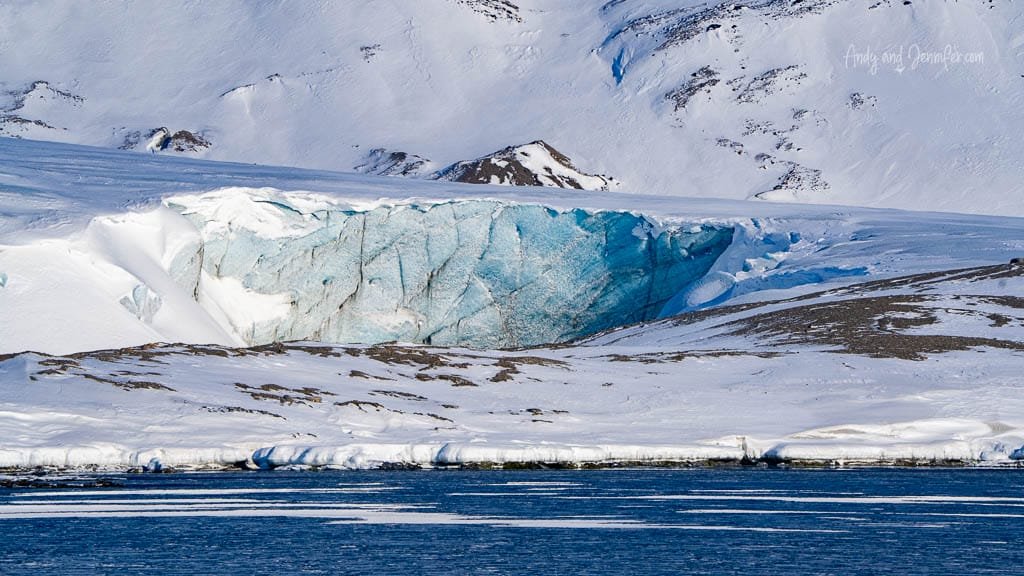 Blue-glowing glacier face emerging from snowy slope