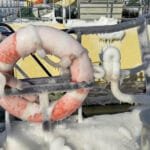Orange life ring frozen in ice on snowy deck of Arctic vessel.