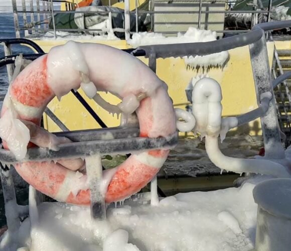 Orange life ring frozen in ice on snowy deck of Arctic vessel.