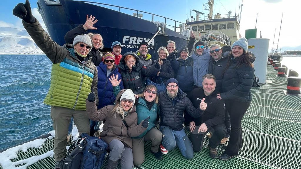 Group of smiling people posing by ship Freya in Arctic marina