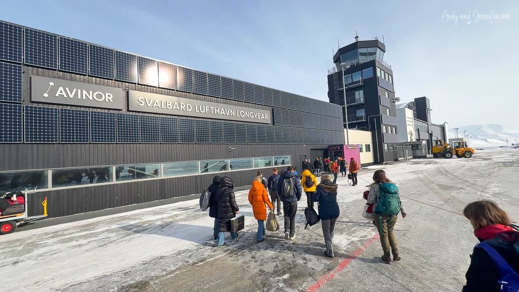 Travelers walk into Svalbard Airport under clear sky.