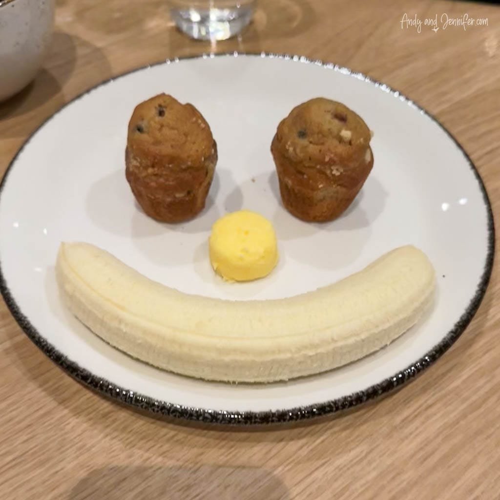 Smiley face made of banana, muffins, and butter on plate